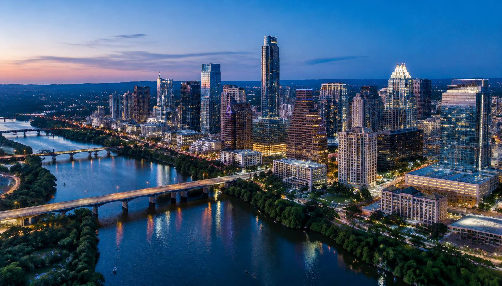 Aerial view of the downtown Austin, Texas skyline at dusk, with Lady Bird Lake and its bridges in the foreground and the Hill Country on the horizon